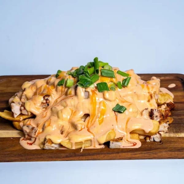 Halal Eatery's loaded fries with chicken, creamy sauce, and chopped green onions on a wooden board.