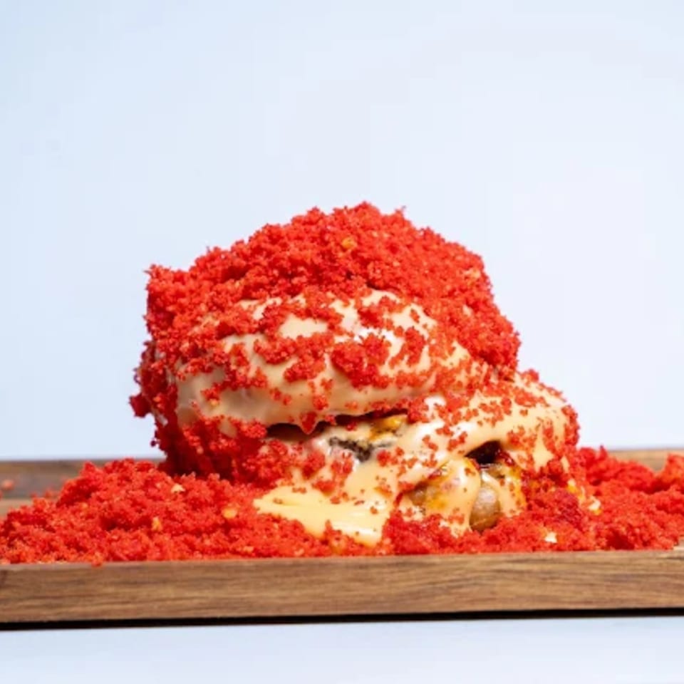 A Halal Eatery burger with white sauce and red crunchy toppings on a wooden board.