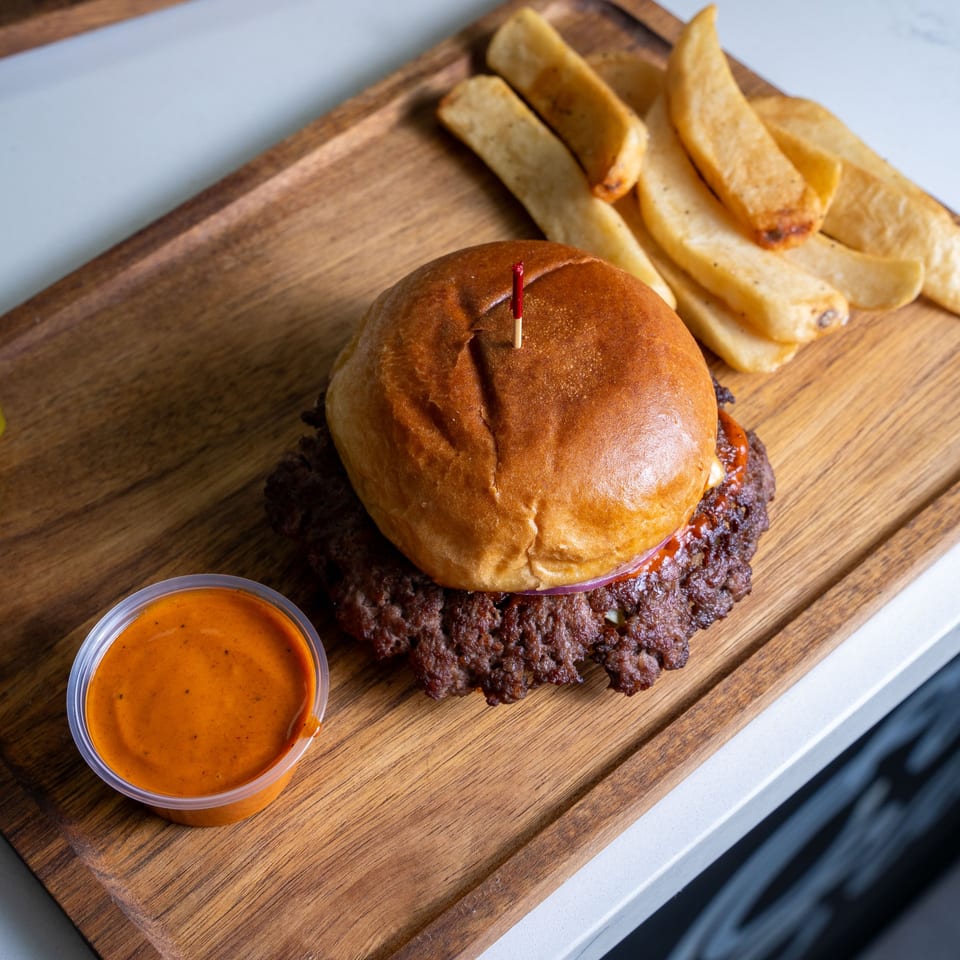 A Halal Eatery smash burger with fries and dipping sauce on a wooden board.
