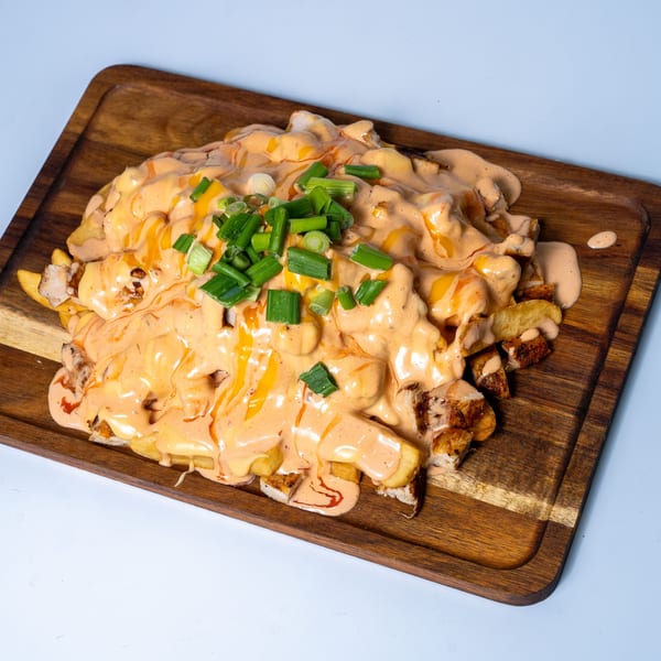 Halal Eatery's loaded fries with melted cheese, creamy sauce, and chopped green onions on a wooden board.