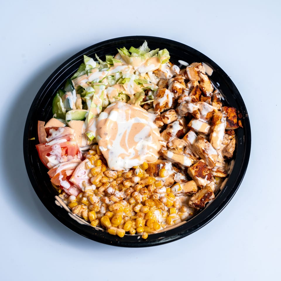 A Halal Eatery chicken and corn bowl with lettuce, tomatoes, and two sauces.