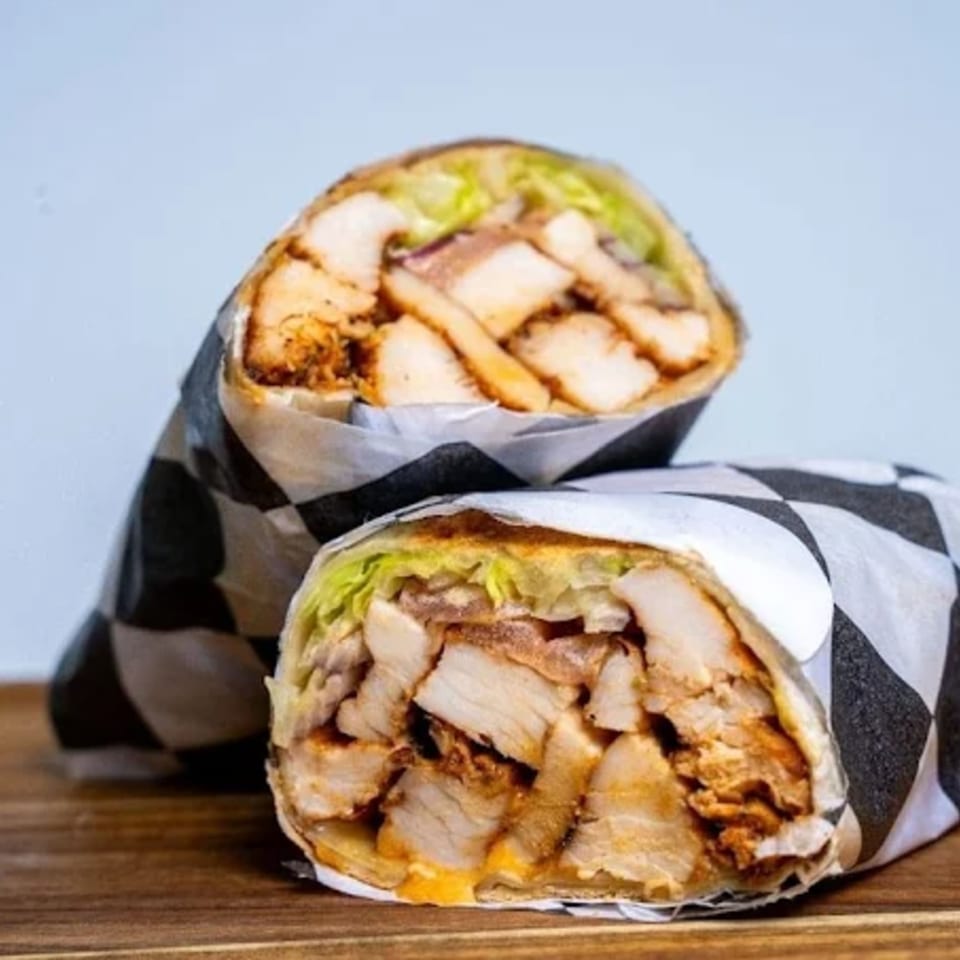 Two Halal Eatery chicken wraps, filled with meat, lettuce, and sauce, on a wooden surface.