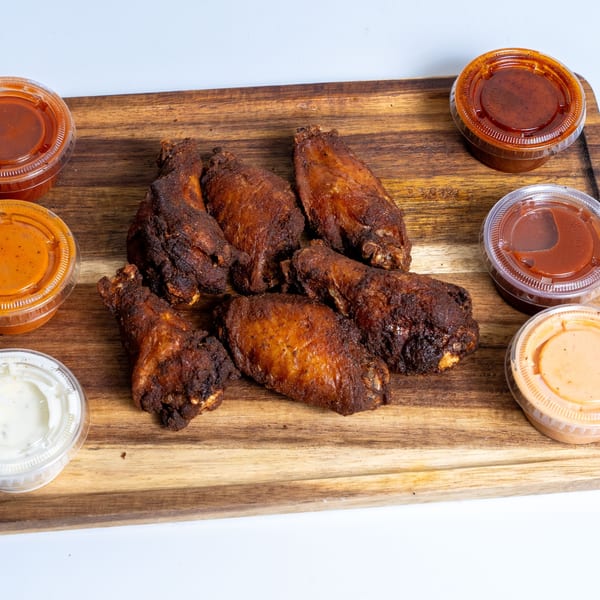 Crispy fried chicken wings with various dipping sauces on a wooden board at Halal Eatery.