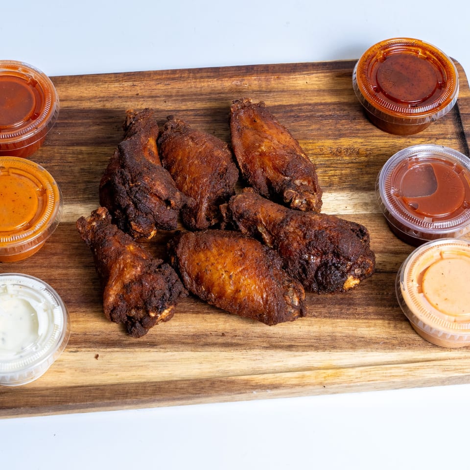Crispy fried chicken wings with various dipping sauces on a wooden board at Halal Eatery.